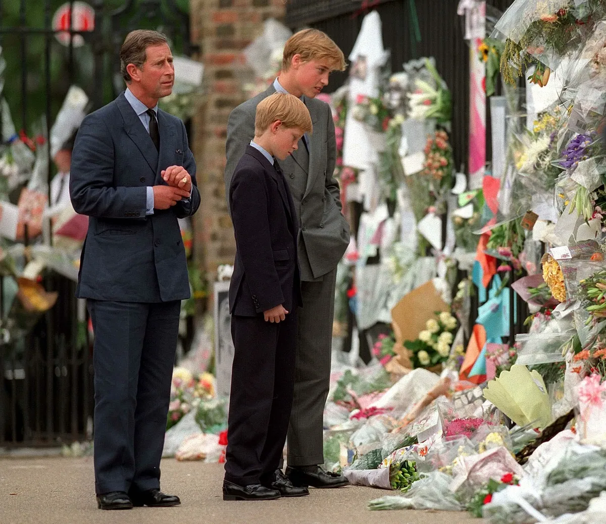 The Prince of Wales, Prince William and Prince Harry look at floral tributes to Diana, Princess of Wales outside Kensington Palace on September 5, 1997 in London, England.