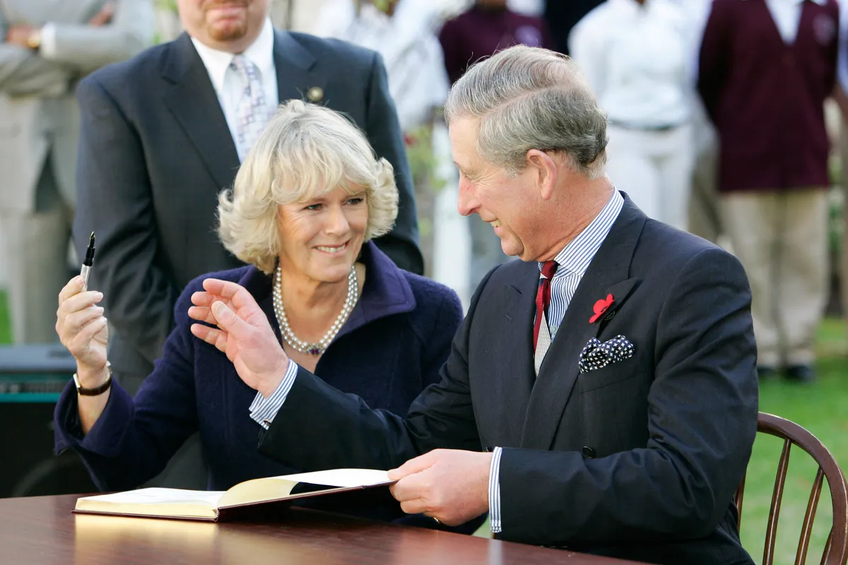 TRH Prince Charles, Prince of Wales and Camilla, Duchess of Cornwall giggle as she is reluctant to return his pen as they sign the visitors' book at SEED School.