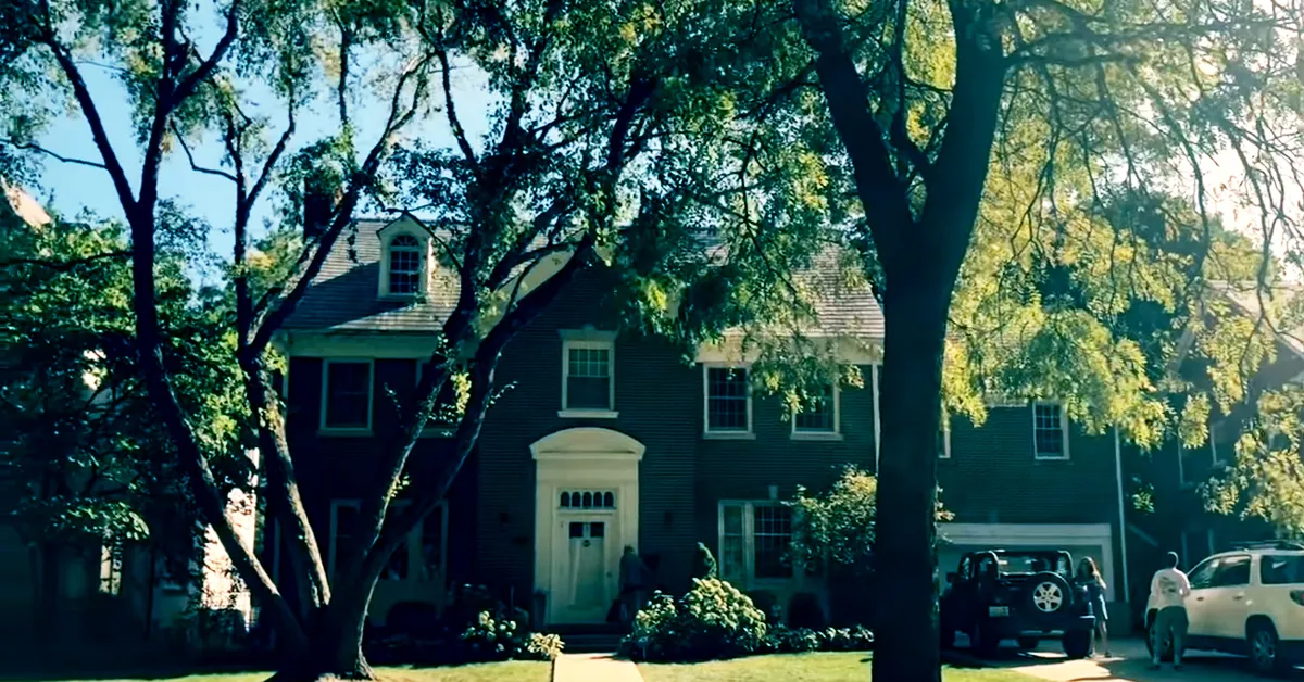 exterior of the house used for sixteen candles surrounded by trees with two cars and people in the driveway