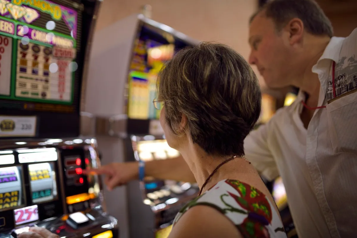 Man explaining readout to a woman on slot machines in a casino. 