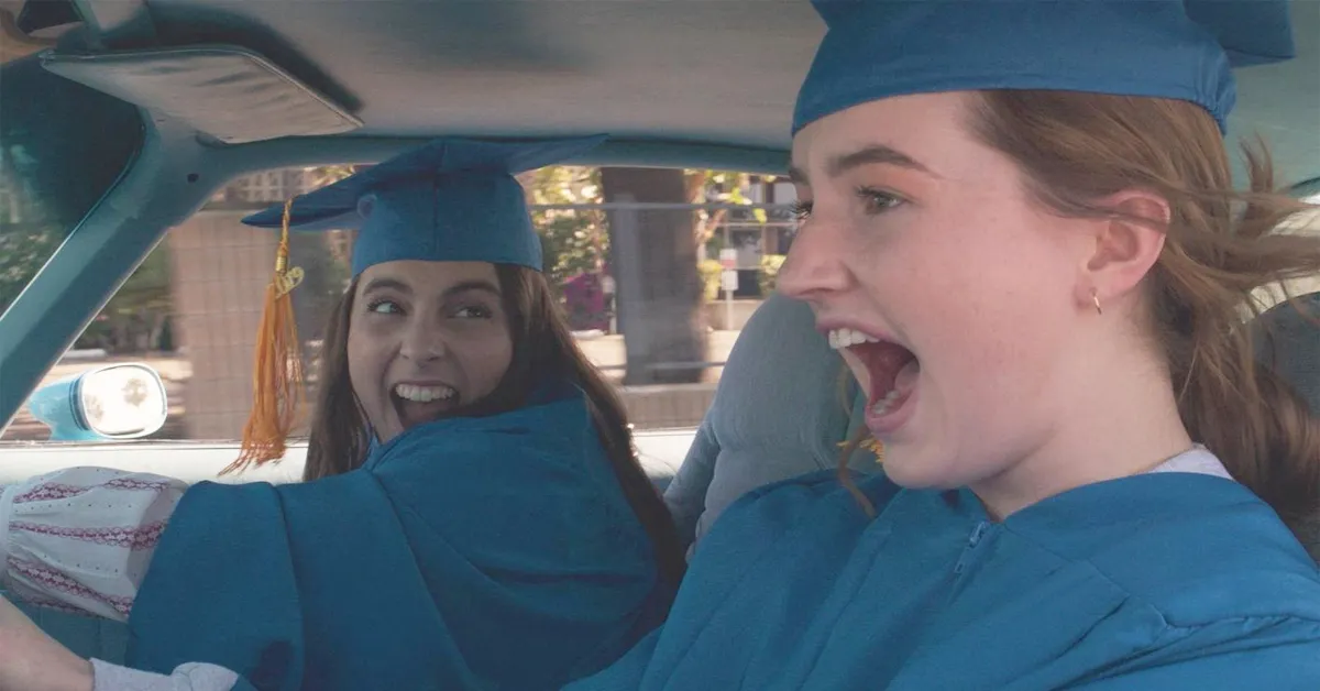 beanie feldstein and kaitlyn dever in graduation caps and gowns driving a car in booksmart