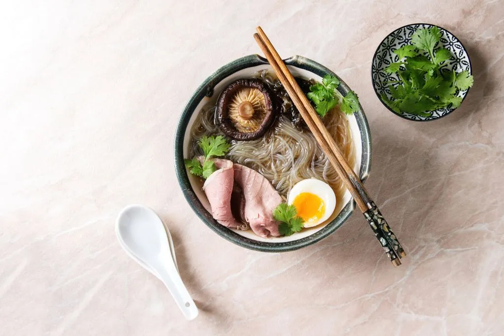 a bowl of ramen with shiitake mushroom, egg, sliced beef, and greens