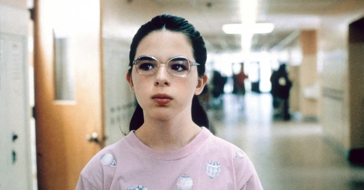 heather matarazzo wearing glasses and a pink shirt in a school hallway in welcome to the dollhouse