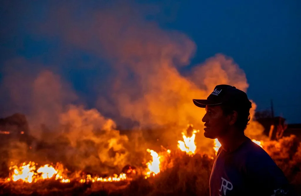 A profile shot of a laborer reveals flames engulfing the land before him.