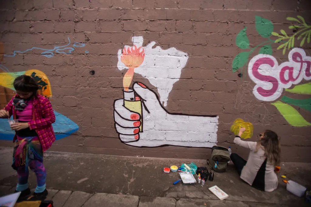 Women paint a brick wall at Cem Minas Na Rua 2019.