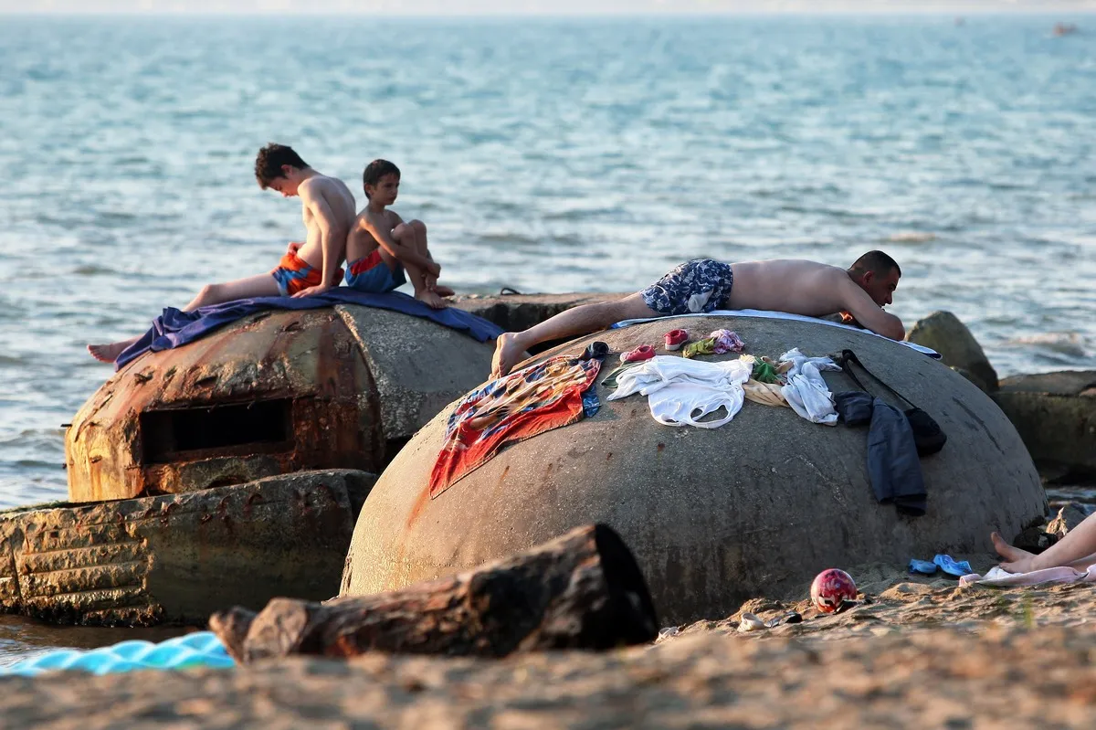 People sunbath atop of decrepit communist era bunkers on the shore in Qerret beach