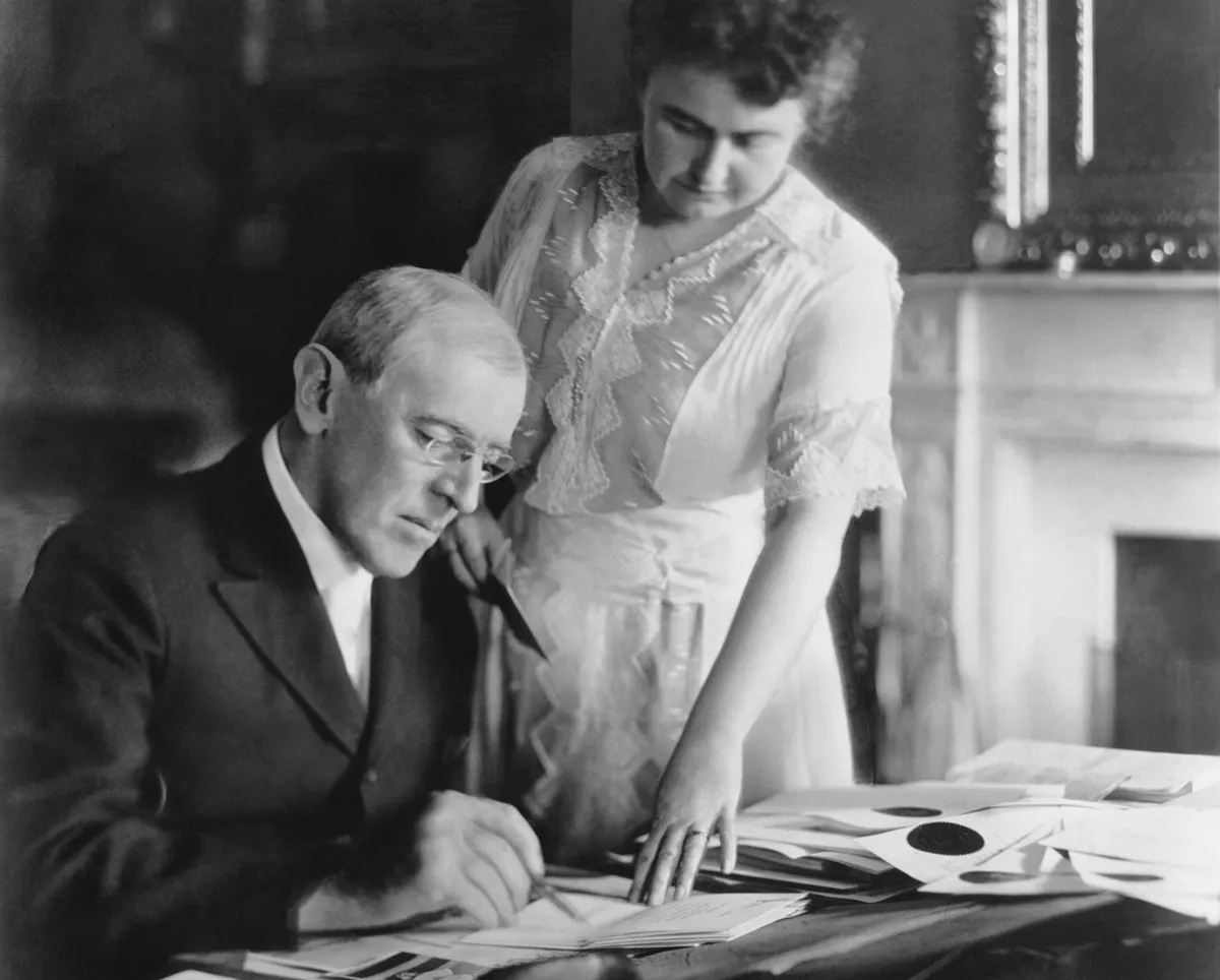 First Lady Edith Wilson assists President Woodrow Wilson at his desk in the White House, 1920