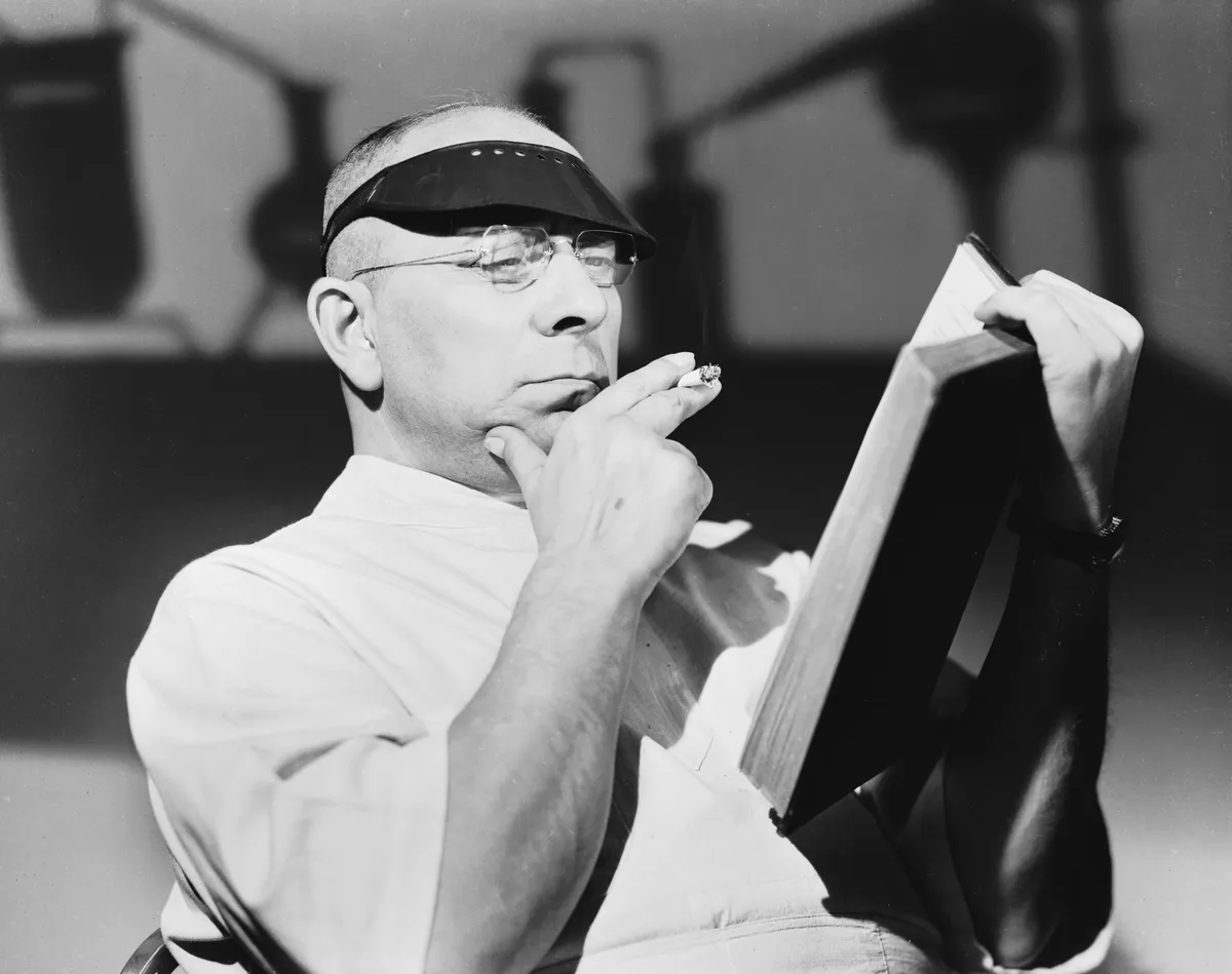 Wearing a sun visor, Austrian actor, screenwriter and director Erich von Stroheim (1885 - 1957) peruses a book during the filming of 'The Lady and the Monster'.