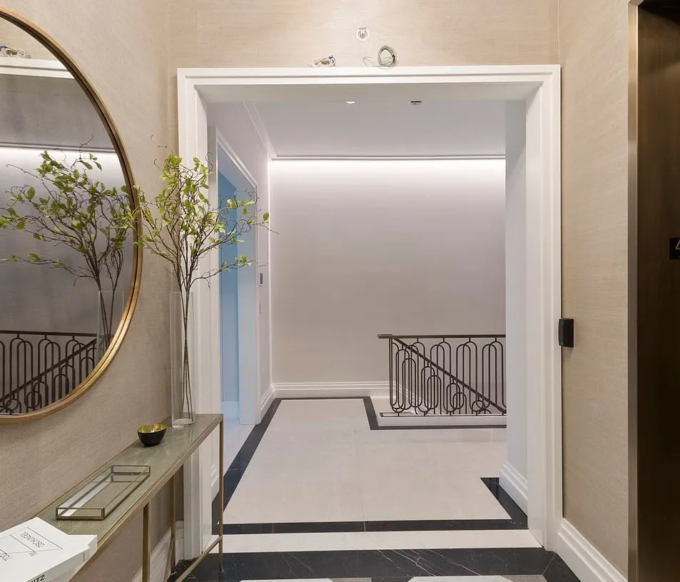 The elevator is to the right, in front of a mirror, entryway table, and modern chandelier.