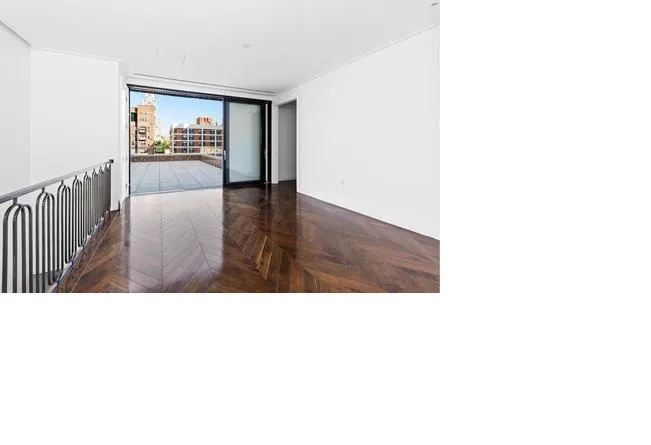 Hardwood floors line a bare space shapped by white walls and a huge sliding glass door, beyond which skyscrapers are in view.