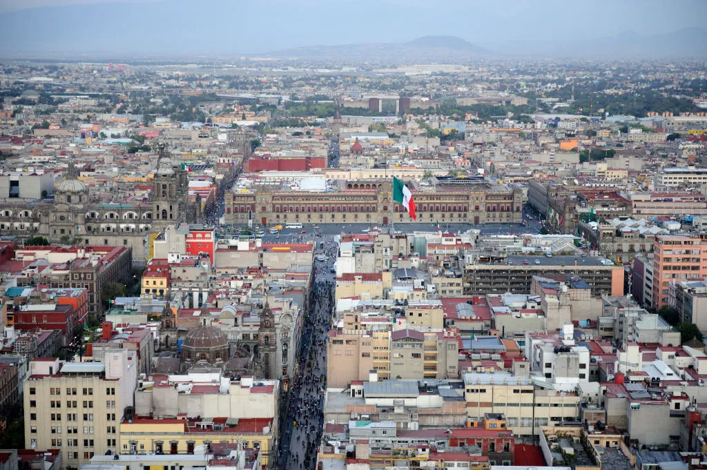 An aerial view of Mexico City shows buildings and a Mexican flag blowing in the wind