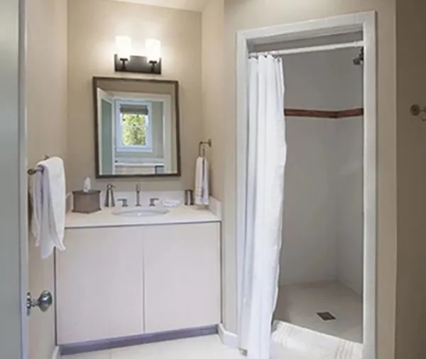 A white bathroom shows a corner shower stall and simple vanity