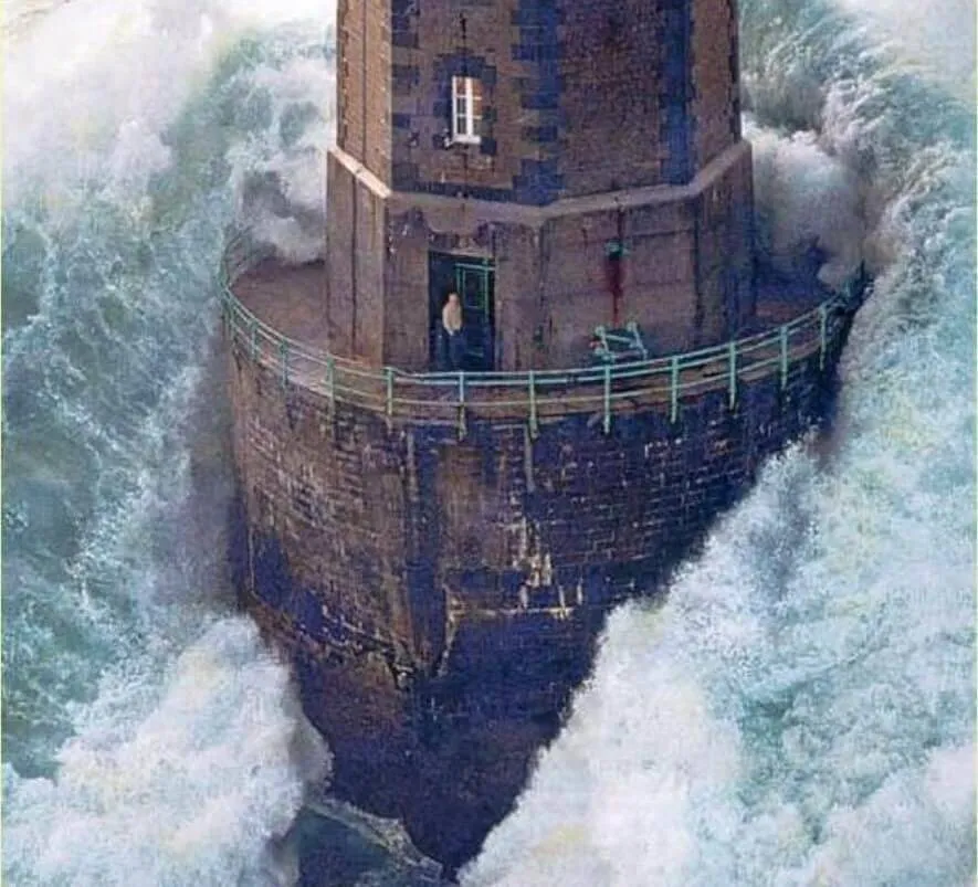 person standing in lighthouse door as large wave hits it