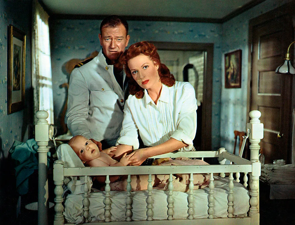 John Wayne and Maureen O'Hara stand over a baby in a crib in a scene from the film 'The Wings Of Eagles
