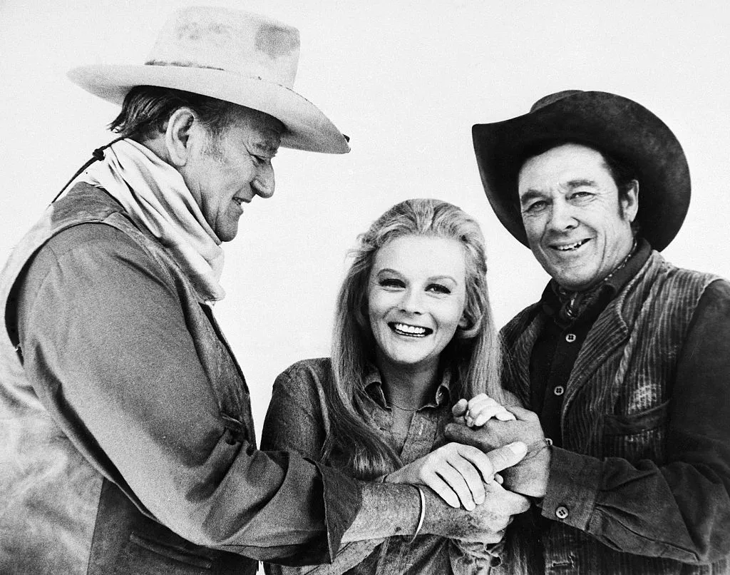 John Wayne, Ann-Margret and Ben Johnson playfully hand-holding during a break in shooting new film on location.