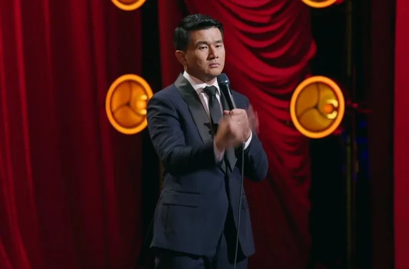 Ronny Chieng wears a straight face while doing a hand motion onstage during his special.