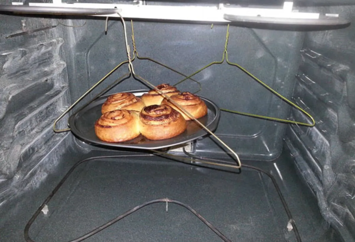 person balances tray of cinnamon buns in oven using clothes hangers