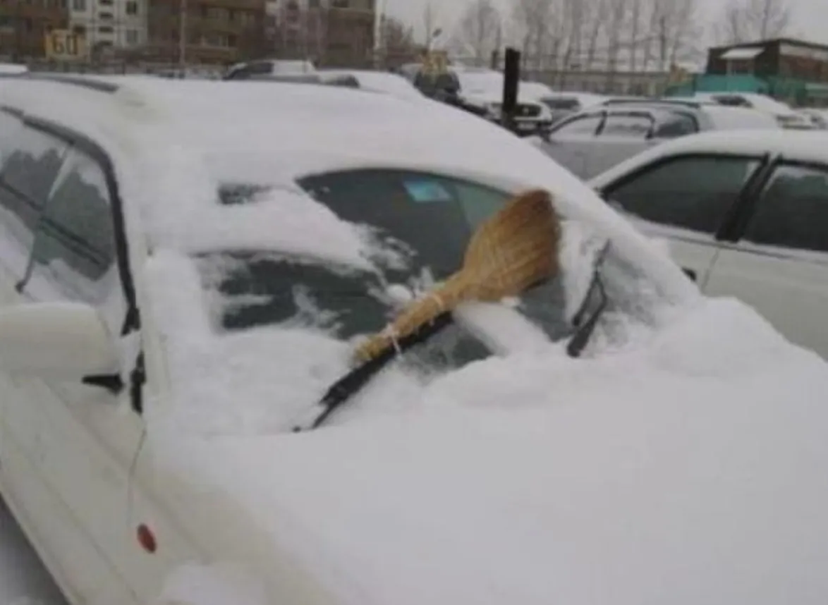 person attaches broom to windshield wiper to clear snow