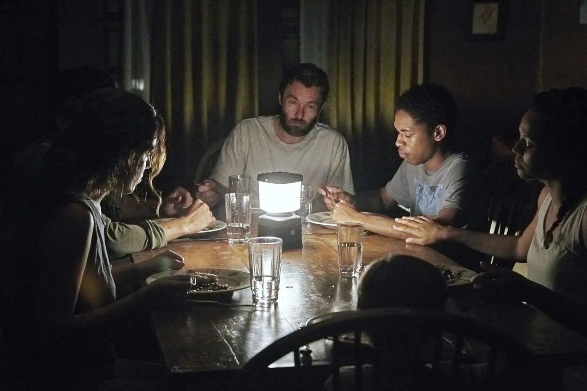 Adults gather around a table that is only lit by a single lamp in its center.