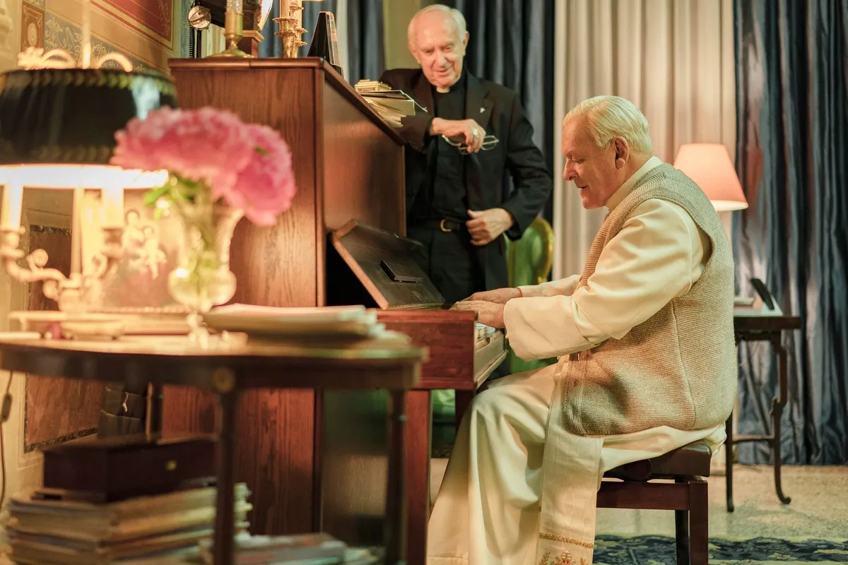 The pope plays piano while the future pope watches and smiles.