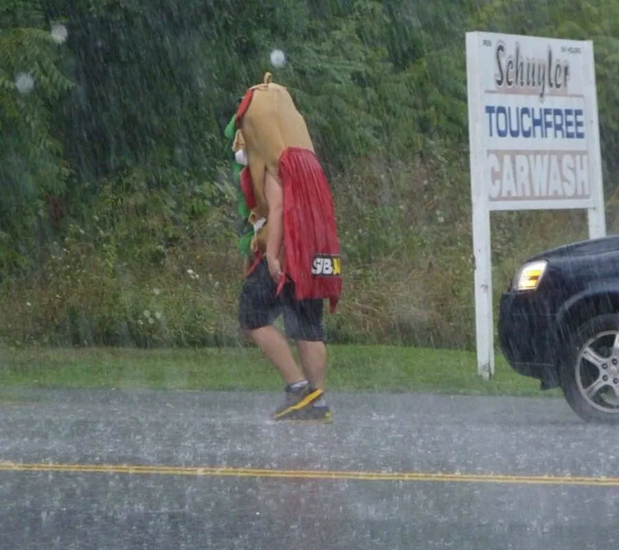 a guy walking around in a hot dog costume while its raining 