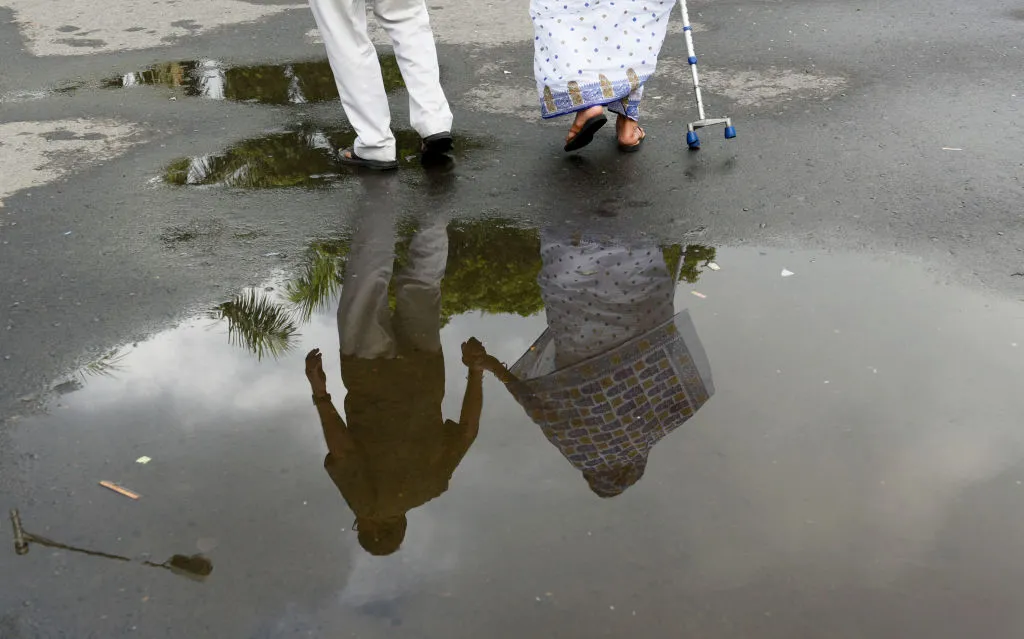 An elderly couple holds hands while crossing a wet street.