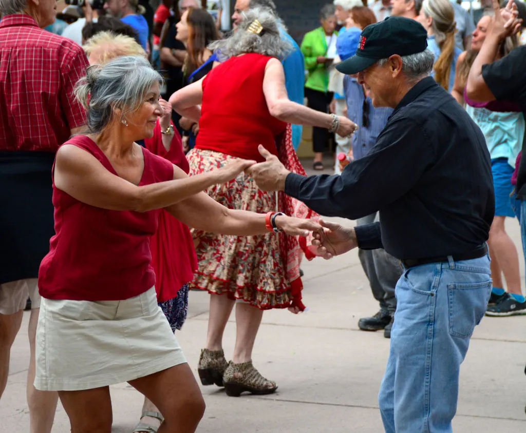 A retired couple dancing outside amongst a crowd.