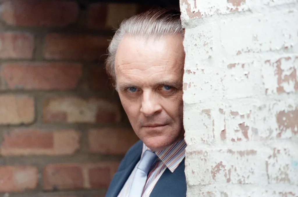 Anthony Hopkins looks grim while peeking from behind a brick wall.