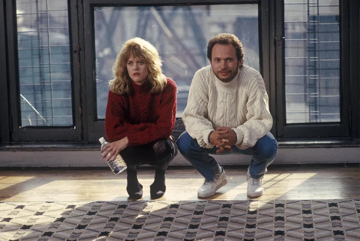 Harry and Sally squat down next to one another in front of a window.