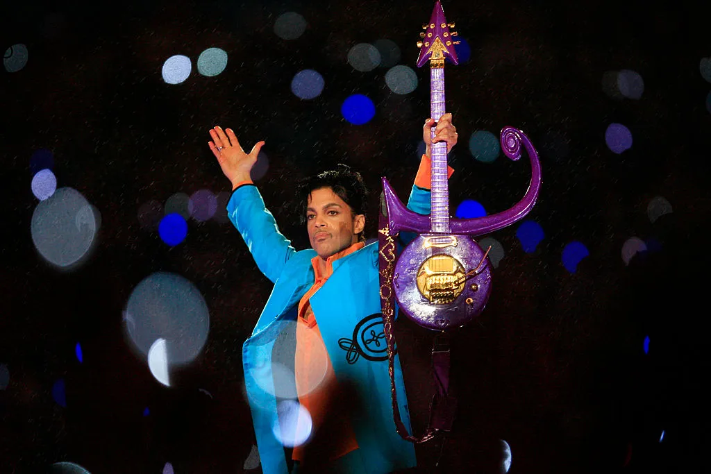 Prince raises his arms and his guitar while performing at the Super Bowl.