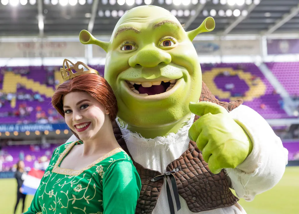 a woman dressed as fiona with a shrek mascot on a soccer field