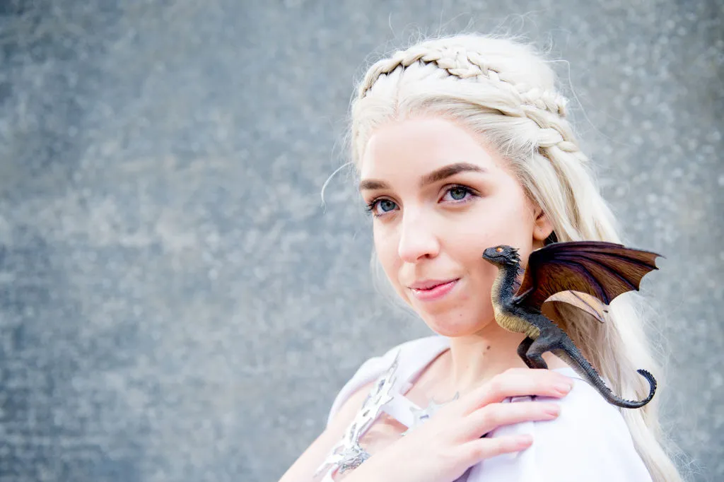 a woman dressed as queen daenerys targaryen with a dragon figurine from game of thrones