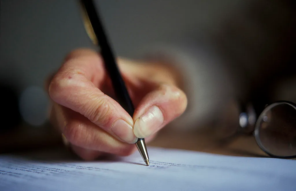 close-up of an elderly person writing with a pen on paper