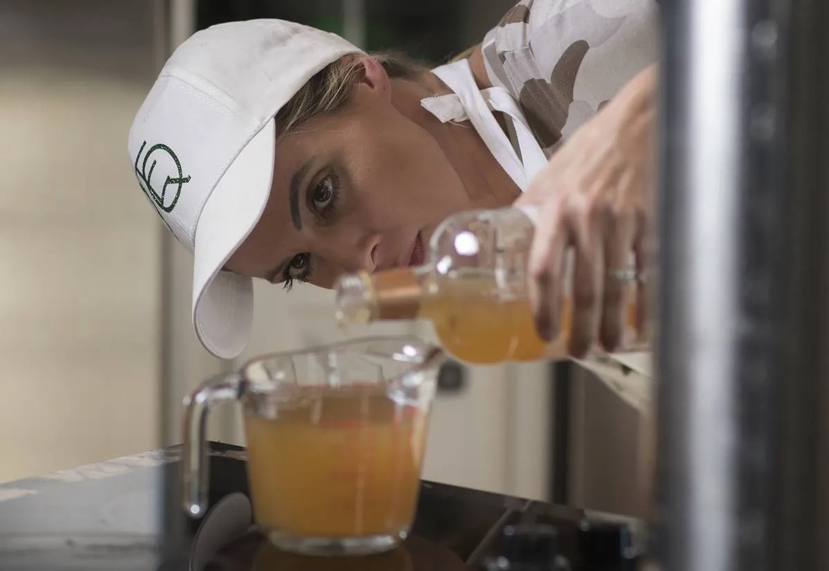 A woman pours apple cider vinegar into elderberry syrup.