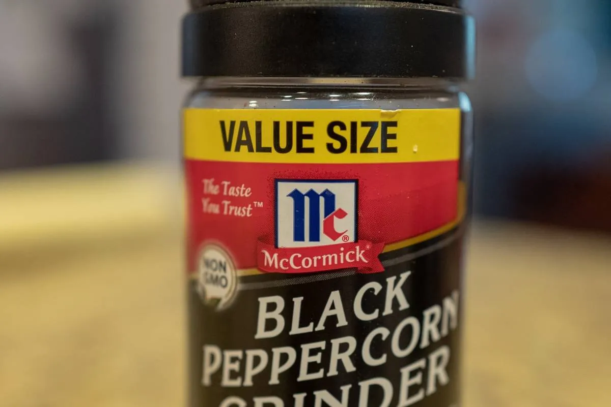 A plastic shaker is filled with black peppercorns.