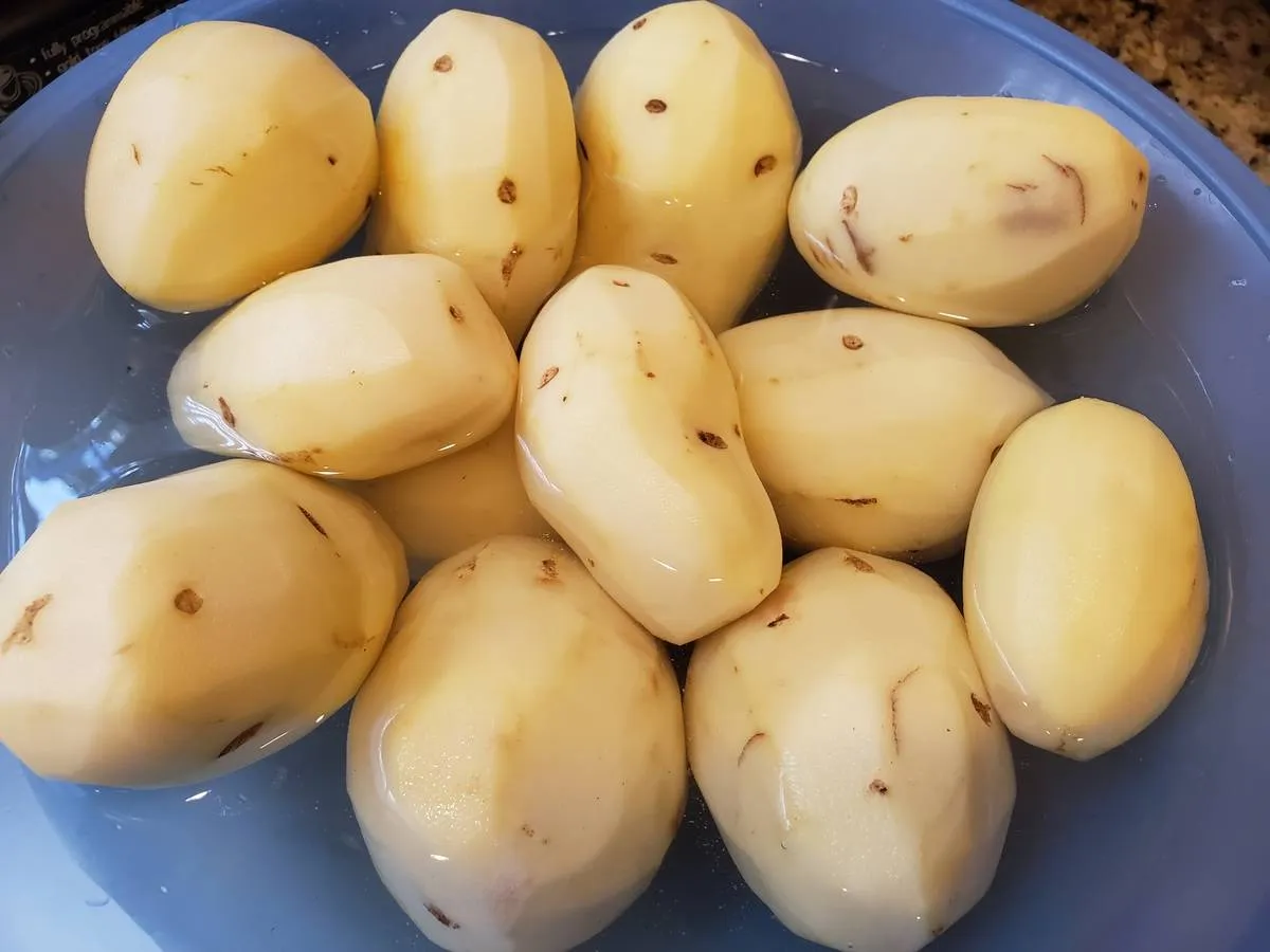 Peeled potatoes soak in water in a blue bowl.