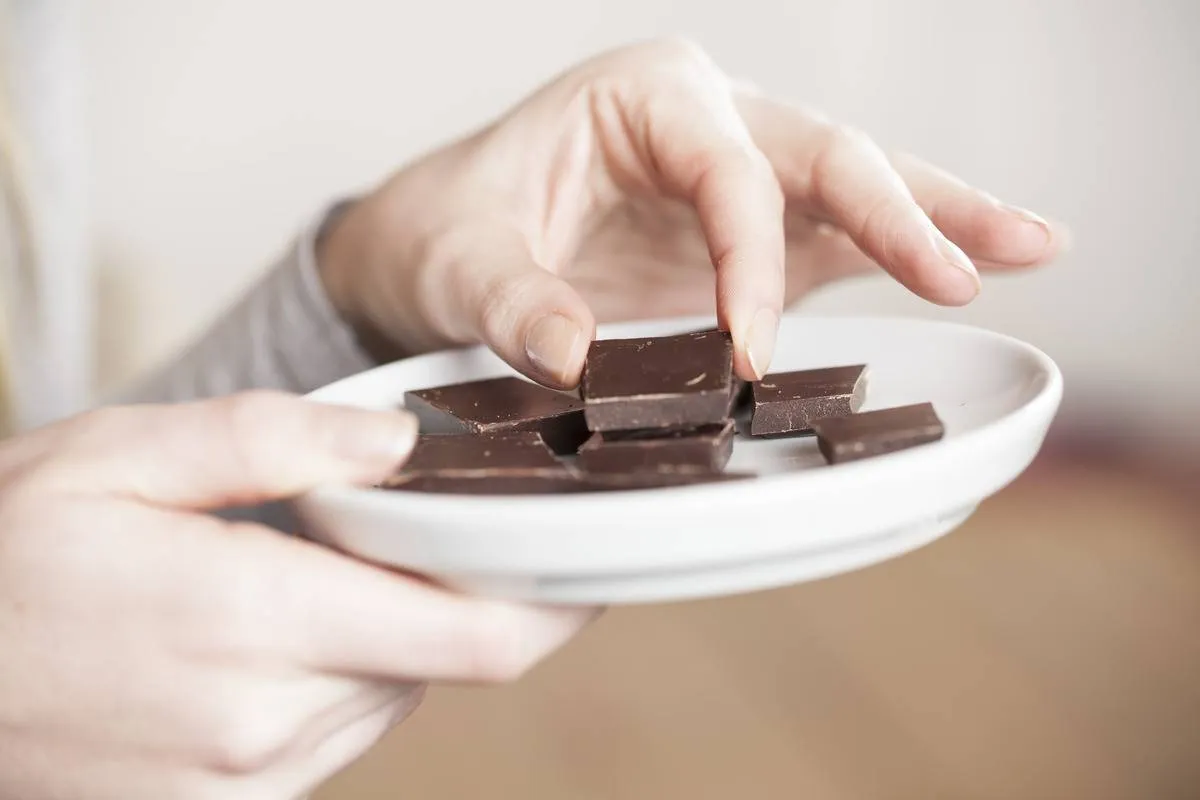 A woman eats squares of chocolate off of a plate.