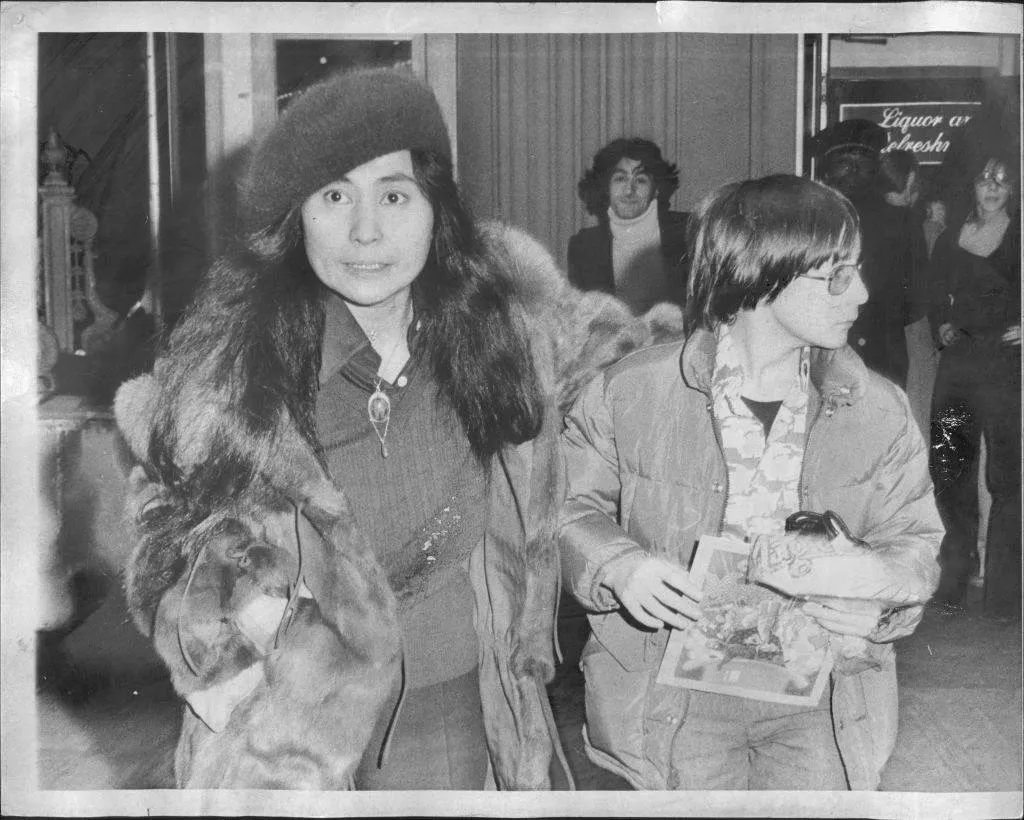 Yoko Ono wears a tense face while walking next to an oblivious teenage Julian.