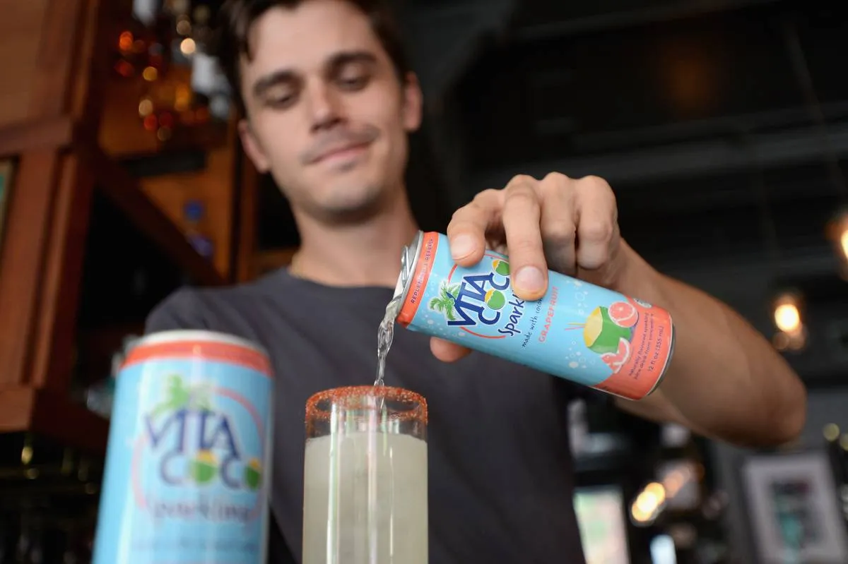 A man pours a sparkling drink with grapefruit and carbonated coconut water into a glass.