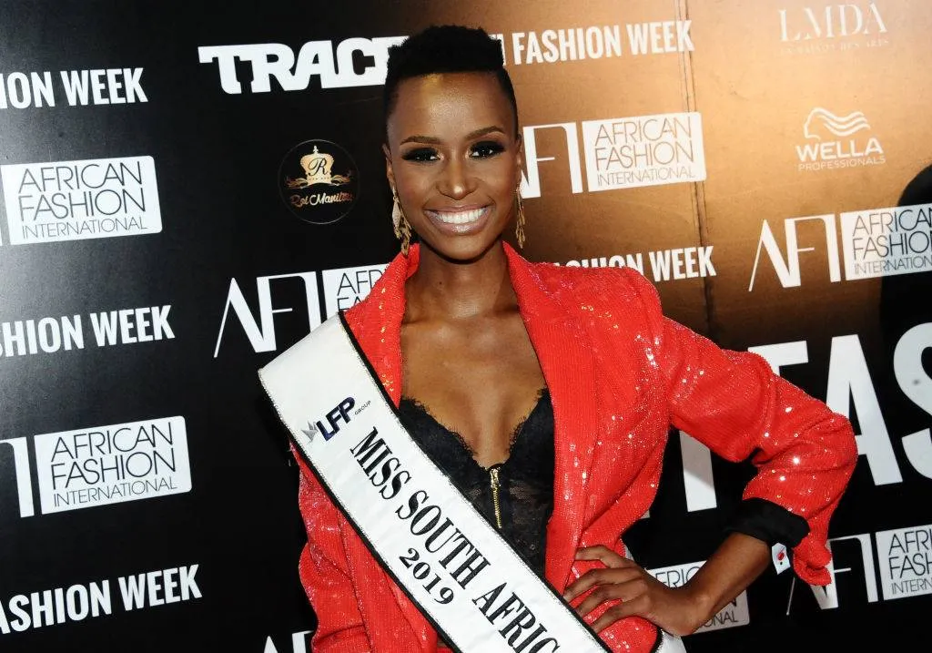 zozibini tunzi wearing her miss south africa sash with a red jacket