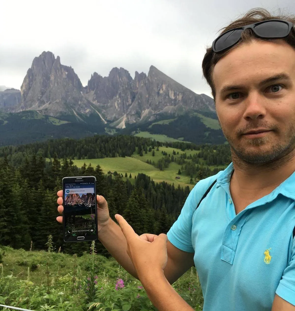 man holding phone of picture of mountains in front of the mountains in real life