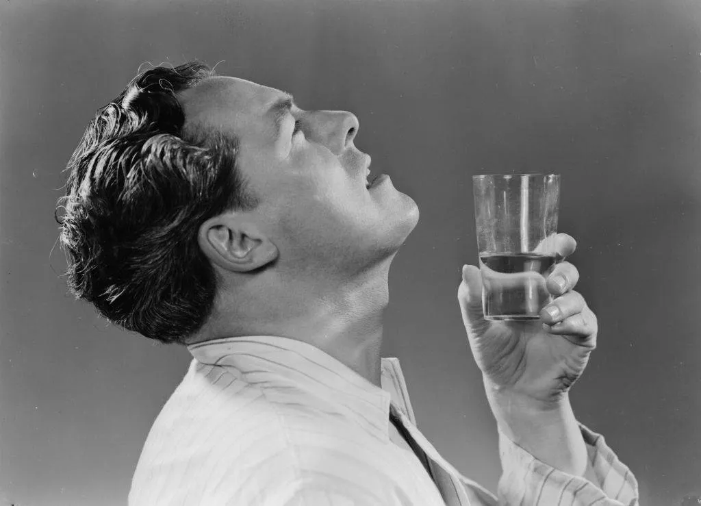 A photograph of a man gargling with a glass of water