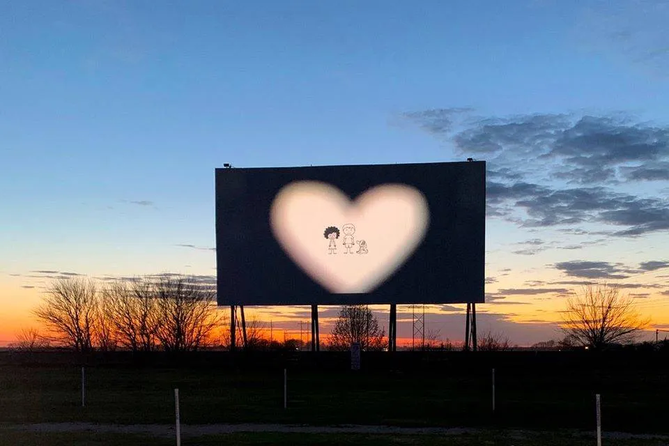 a drive-in at sunset with a heart on screen