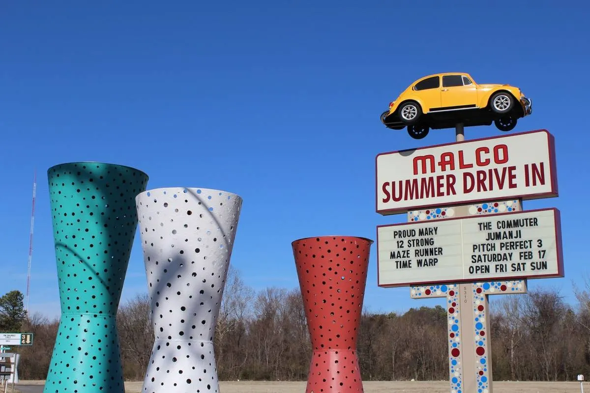 a malco summer drive in sign with a yellow car and colorful sculptures