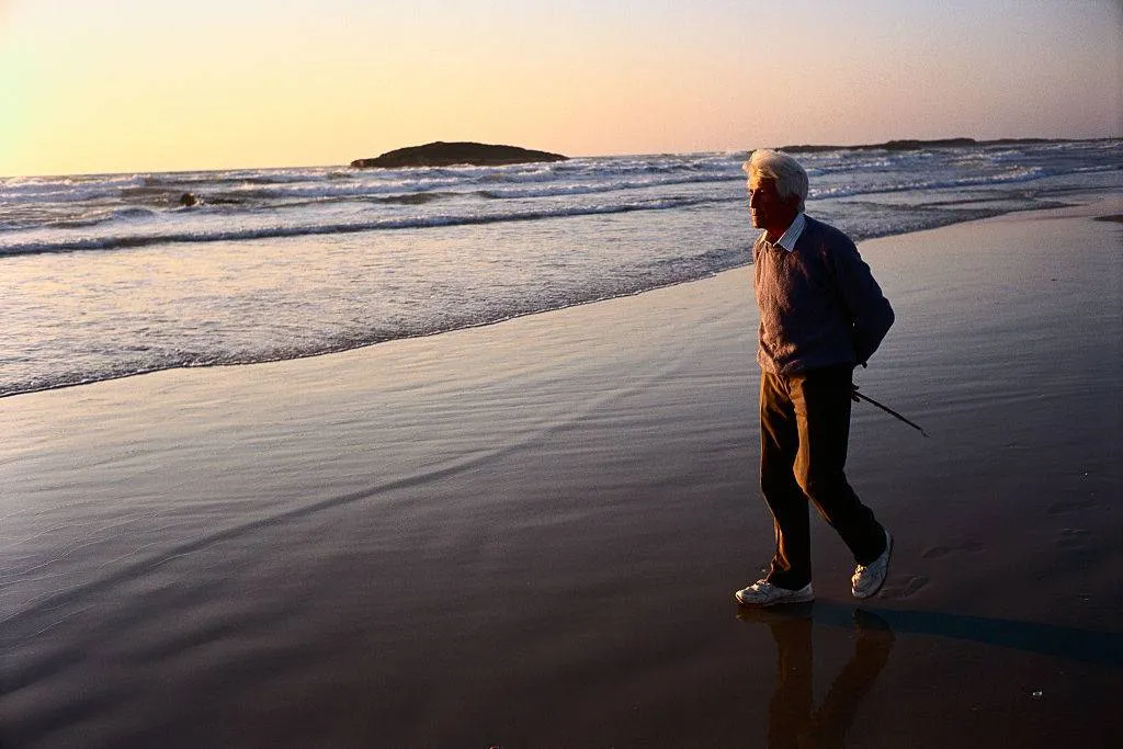 An old man walks on the beach.
