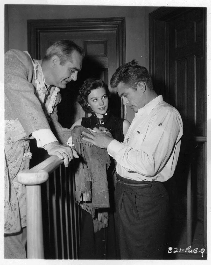 Jim Backus and Natalie Wood watch as James Dean autographs a jacket during a break from shooting the film 'Rebel Without A Cause'