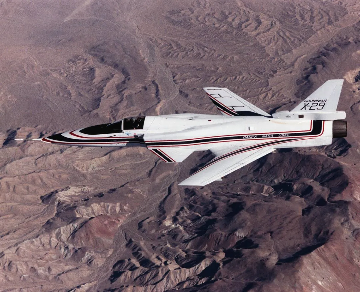 The Grumman X-29A flies over a mountain range.