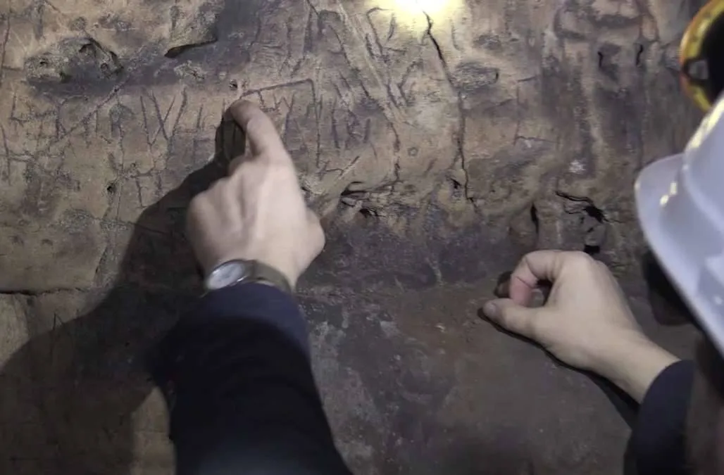 a person pointing to markings on the dirt walls