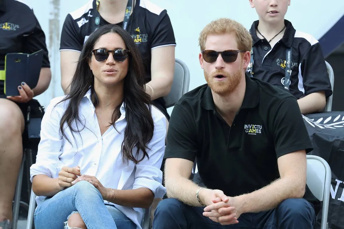 Meghan Markle watches the Invictus Games while wearing a white collared shirt and jeans.
