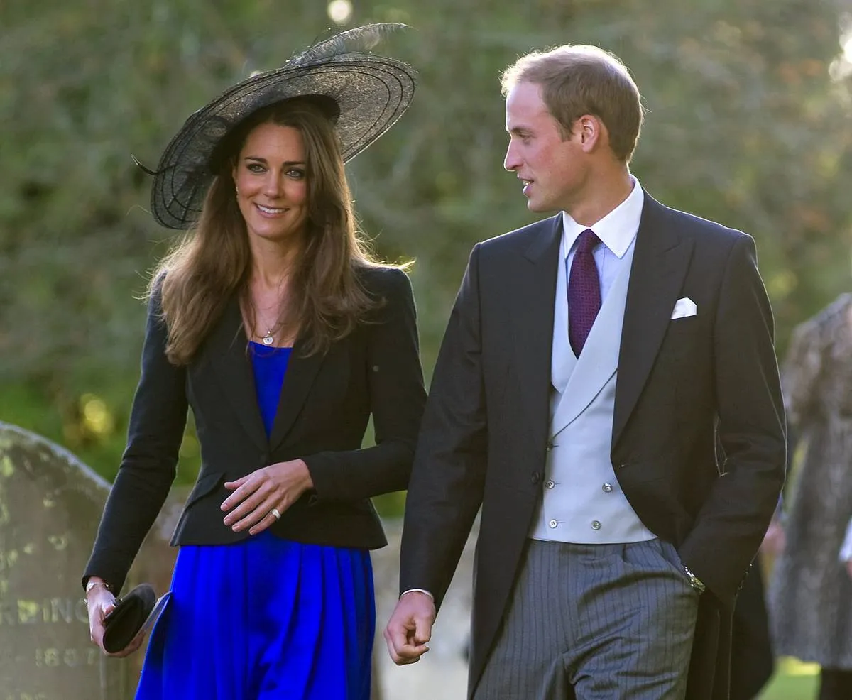 While walking with Prince William, Kate Middleton wears a blue dress with a black blazer and hat.